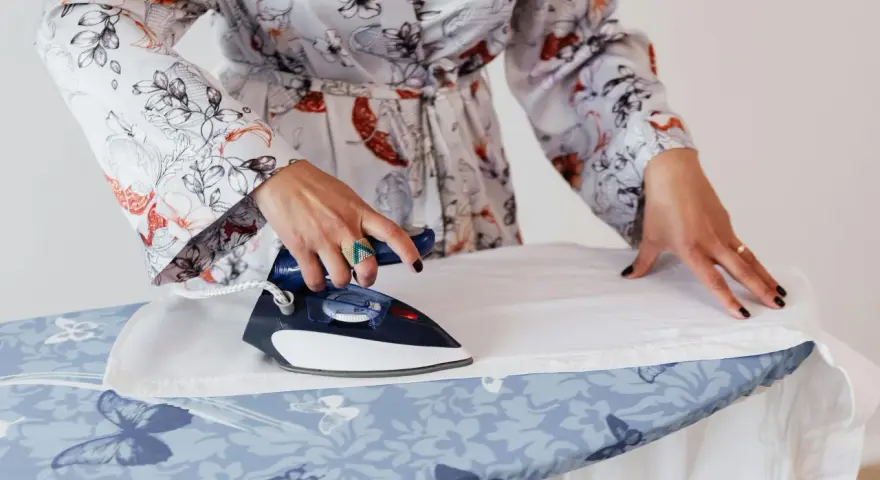 Mujer con bata estampada plancha lino blanco a mano sobre tabla con mariposas.