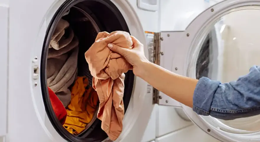 Mano saca ropa de lavadora. Es hora de limpiar lavadora a 90 grados para desinfectarla.