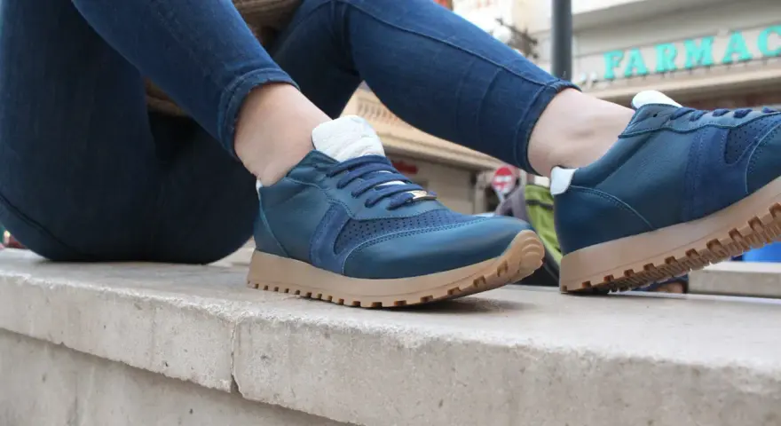 Un hombre luce unas zapatillas azules con cordones y suela de goma, combinadas con vaqueros oscuros.