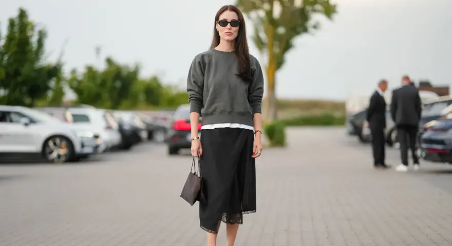 Mujer con falda satinada y zapatillas, bolso marrón y gafas de sol.