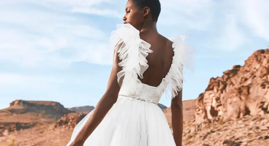 Novia con vestido blanco vaporoso, con volantes en los hombros, ideal para vestidos novia ibiza. Paisaje desértico al atardecer.