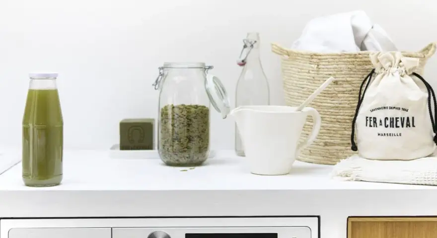 Botella verde, jabón, frasco con hierbas, jarra y bolsa de tela. Ilustra los componentes de los detergentes y sus funciones.