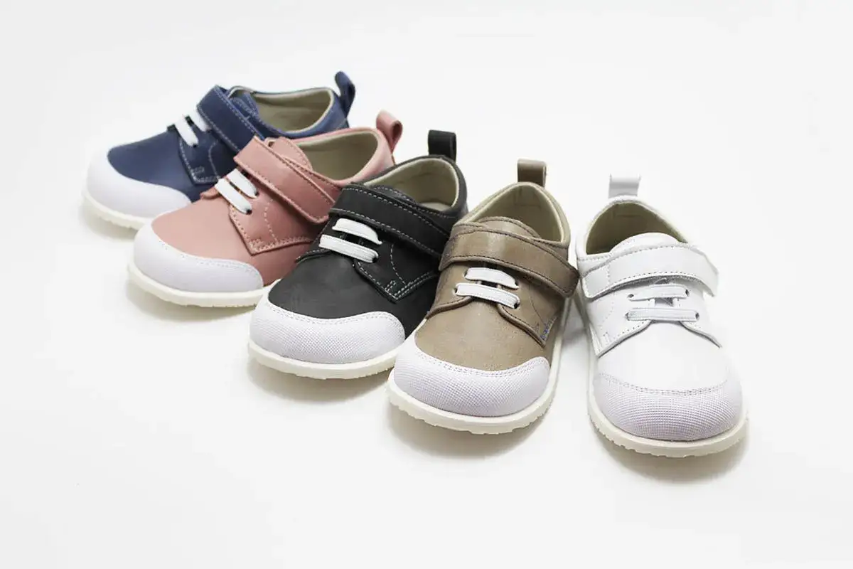Cinco pares de zapato respetuoso para niños en colores azul marino, rosa, negro, marrón y blanco, con suelas blancas y cierres de velcro.