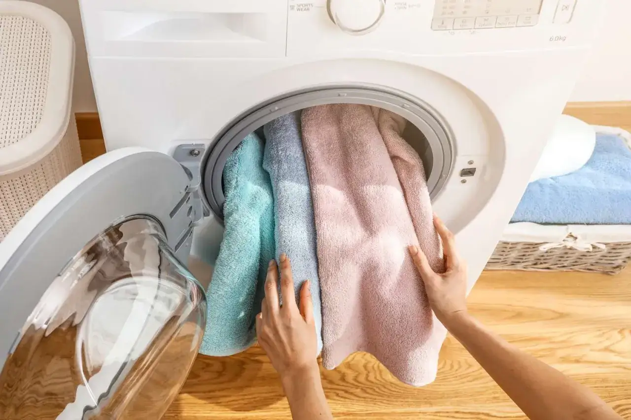 Manos cargando toallas de colores en una lavadora.