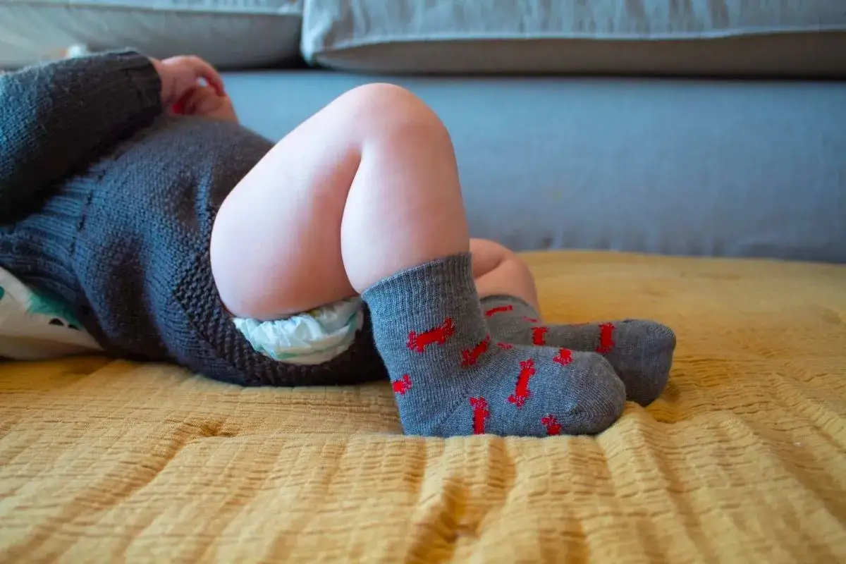 Beb&eacute; reci&eacute;n nacido con pa&ntilde;al y su&eacute;ter oscuro, listo para poner calcetines grises con dibujos rojos.