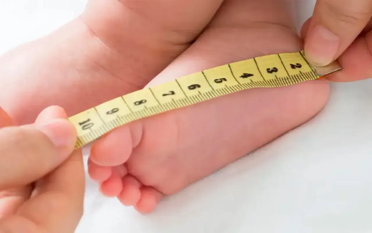 Midiendo el pie de un beb&eacute; para determinar la talla ni&ntilde;o 3 a&ntilde;os. La cinta m&eacute;trica amarilla muestra cent&iacute;metros.