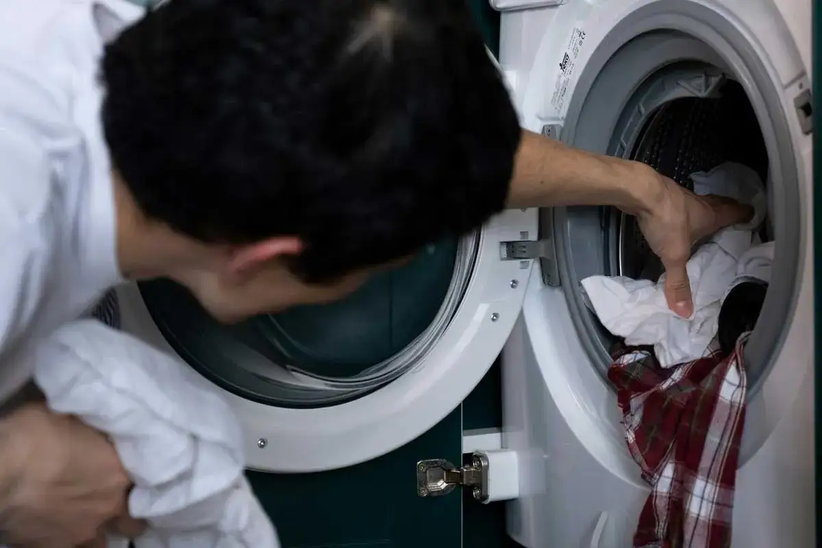 Hombre mete ropa a lavadora. ¡Cuidado! el bicarbonato estropea la ropa de color, podría dañar tu camisa a cuadros.