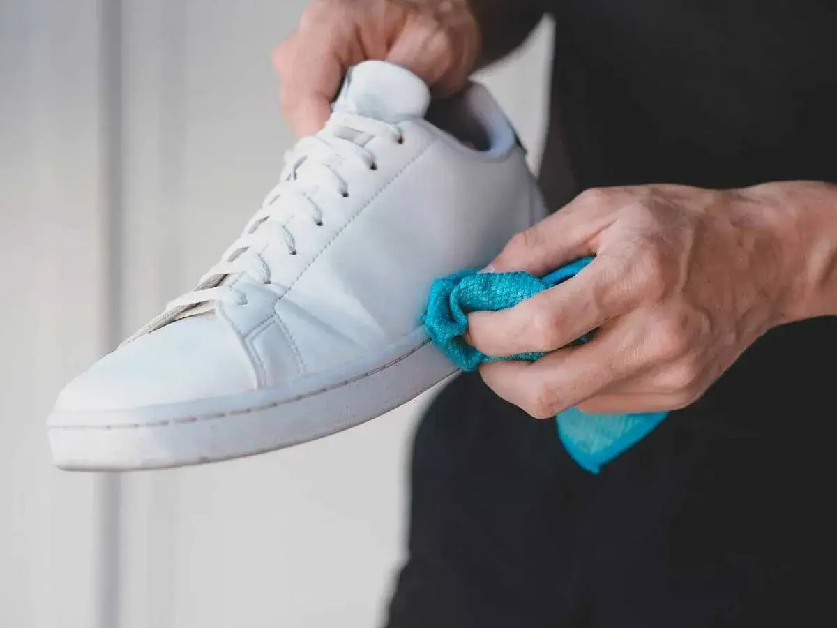 Manos limpiando un zapato de piel clara con un paño azul. Guía rápida: como limpiar zapatos de piel clara.
