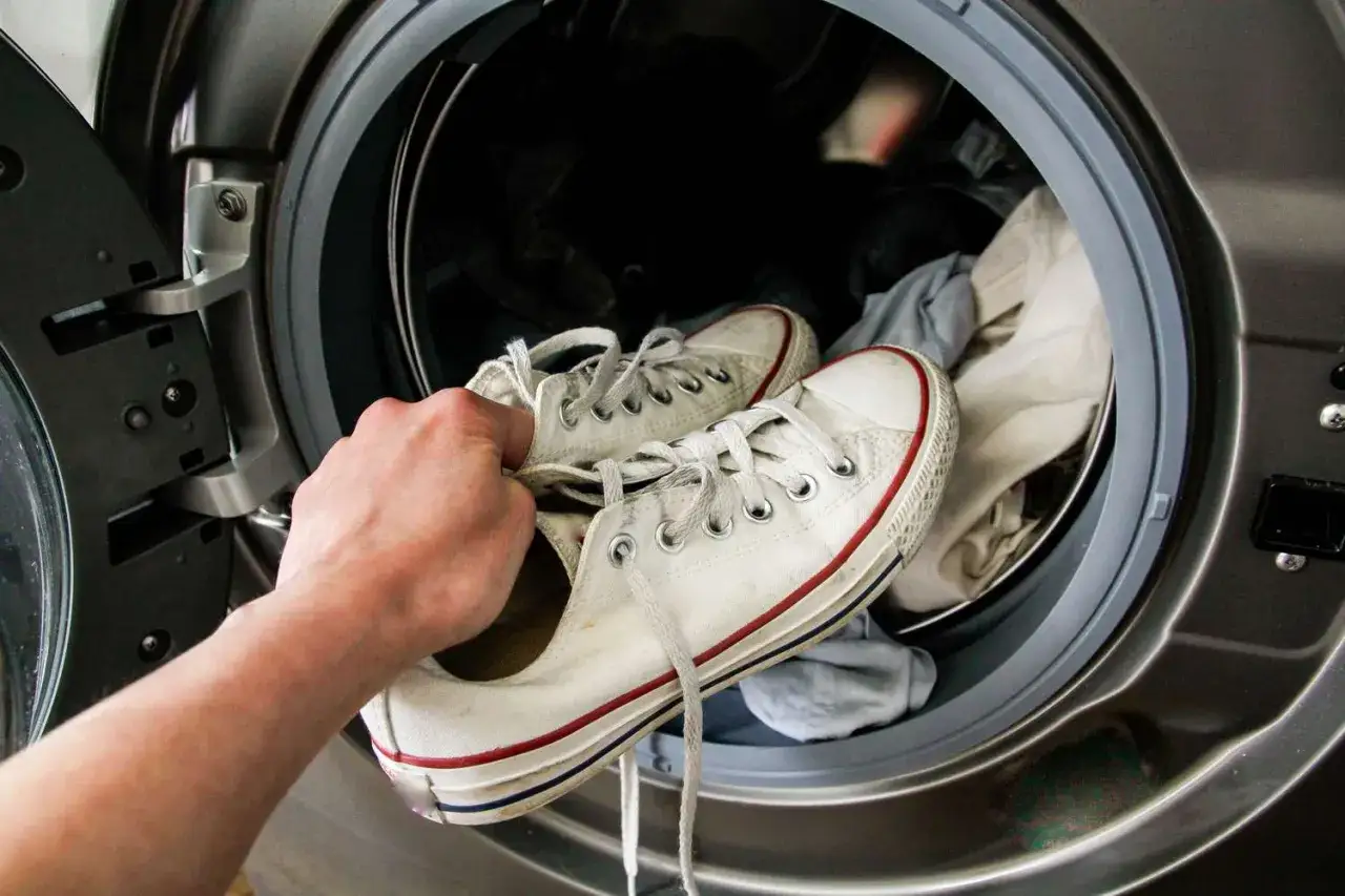 Mano mete zapatillas blancas en lavadora. Aprende como lavar zapatillas en la lavadora para dejarlas como nuevas.