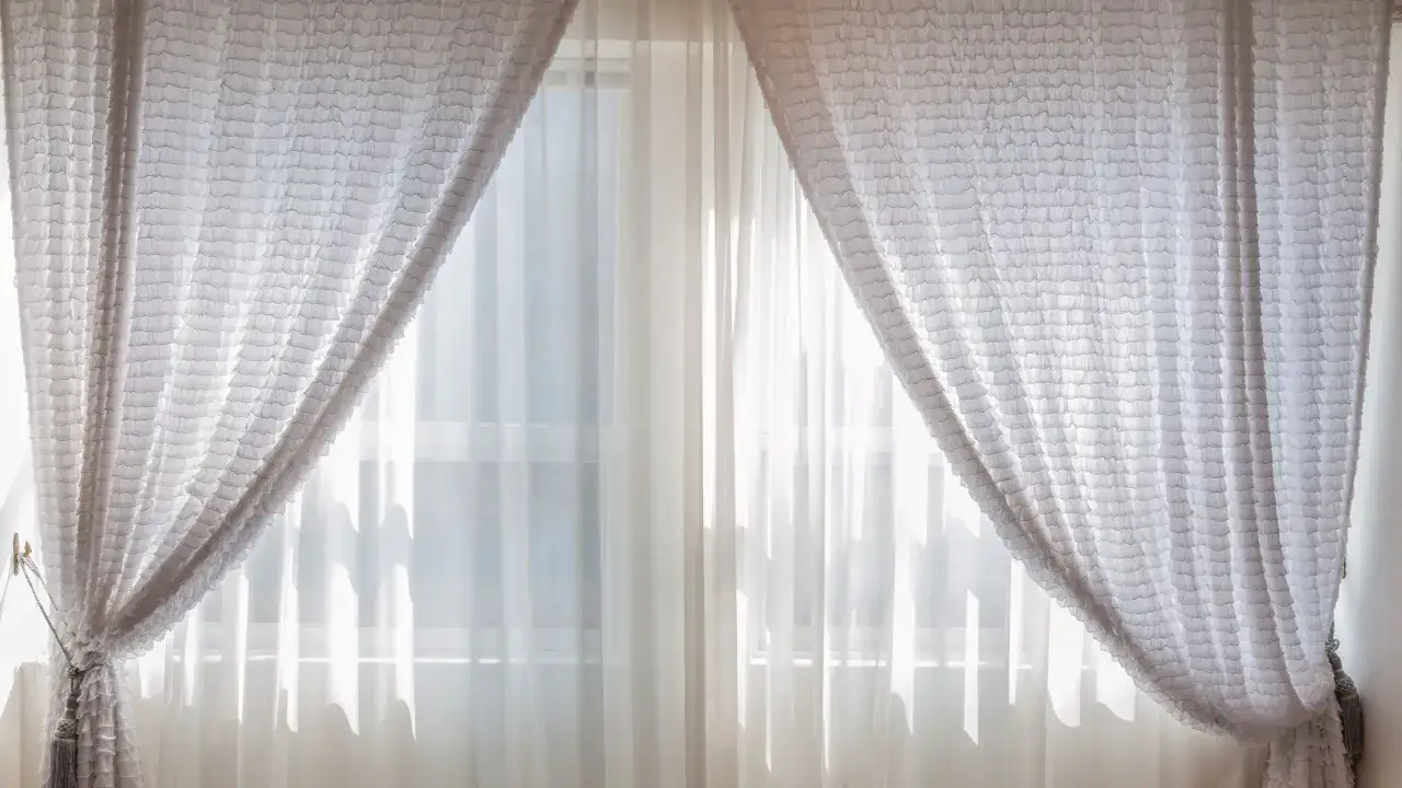 Cortinas blancas con volantes, listas para lavar, cuelgan de una ventana, dejando pasar la luz.
