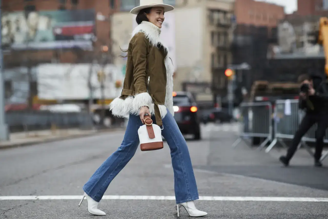 Mujer con sombrero y chaqueta de borrego, luciendo botines blancos por fuera del pantal&oacute;n acampanado.