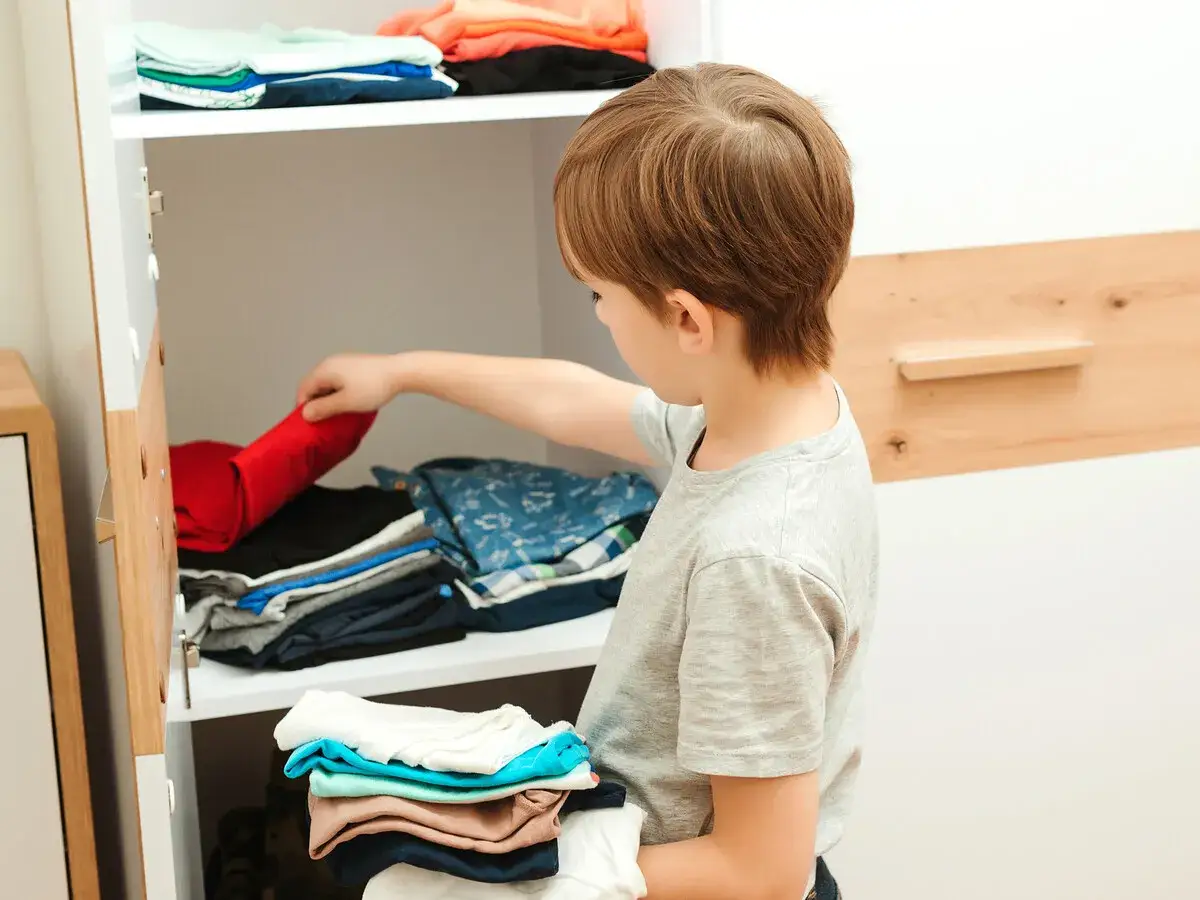Niño de talla 10 años organiza su armario, doblando ropa.