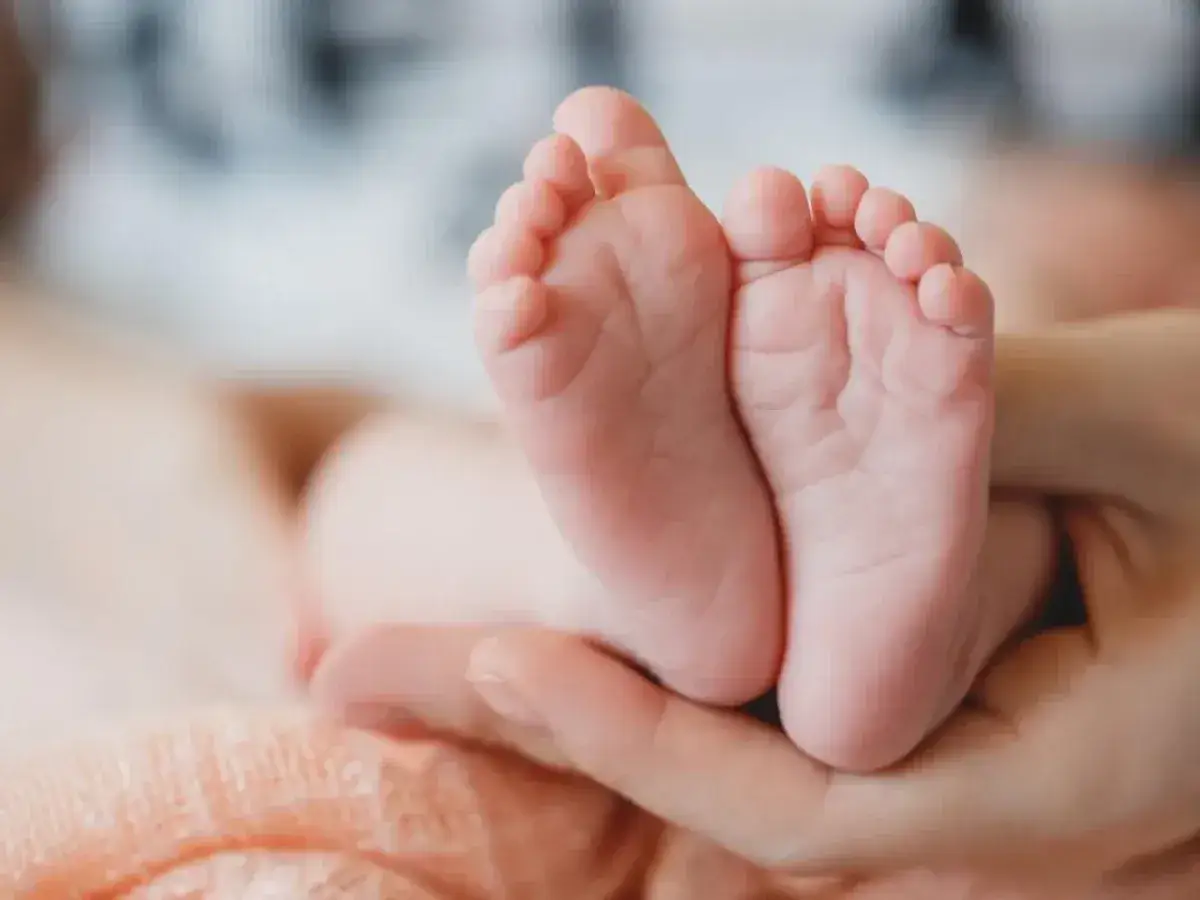 Manos adultas sostienen los pequeños pies de un bebé. A mi bebé le sudan los pies, pero son tan adorables.