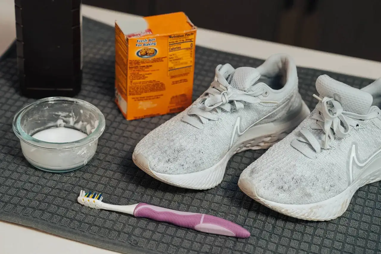 Preparativos para limpiar zapatillas: bicarbonato, cepillo y un par de zapatillas blancas sucias.