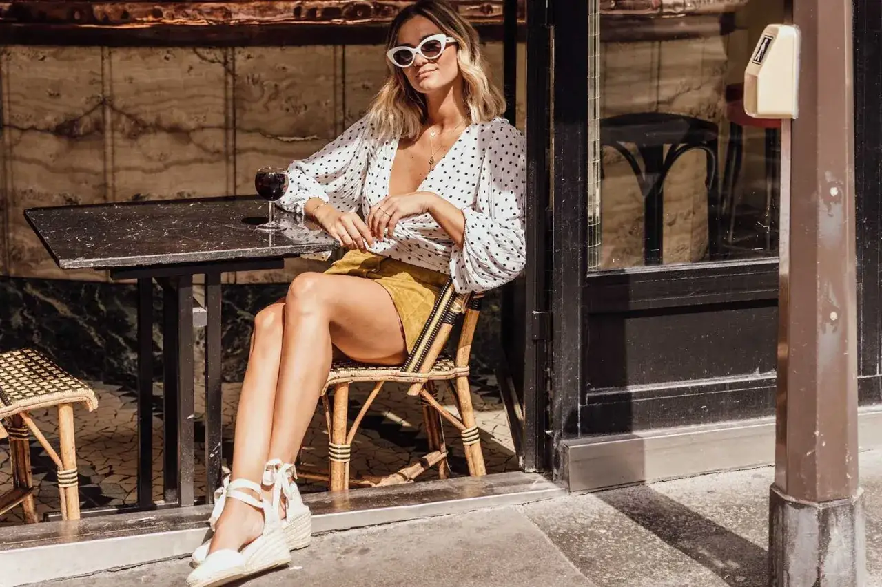 Chica con look veraniego y alpargatas de cu&ntilde;a, sentada en una terraza con una copa de vino.