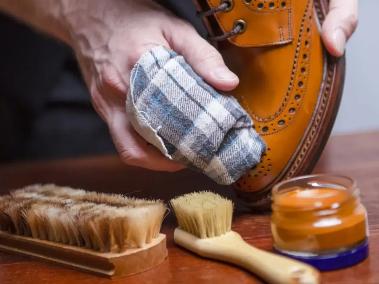Cómo limpiar zapatos de piel: mano con paño puliendo zapato, cepillos y crema para calzado.
