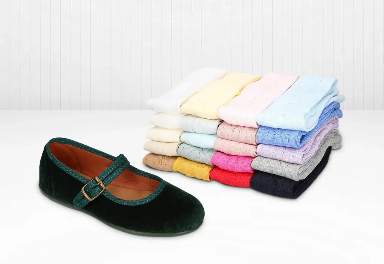 Merceditas verdes de terciopelo junto a una pila de calcetines de ni&ntilde;a en muchos colores.