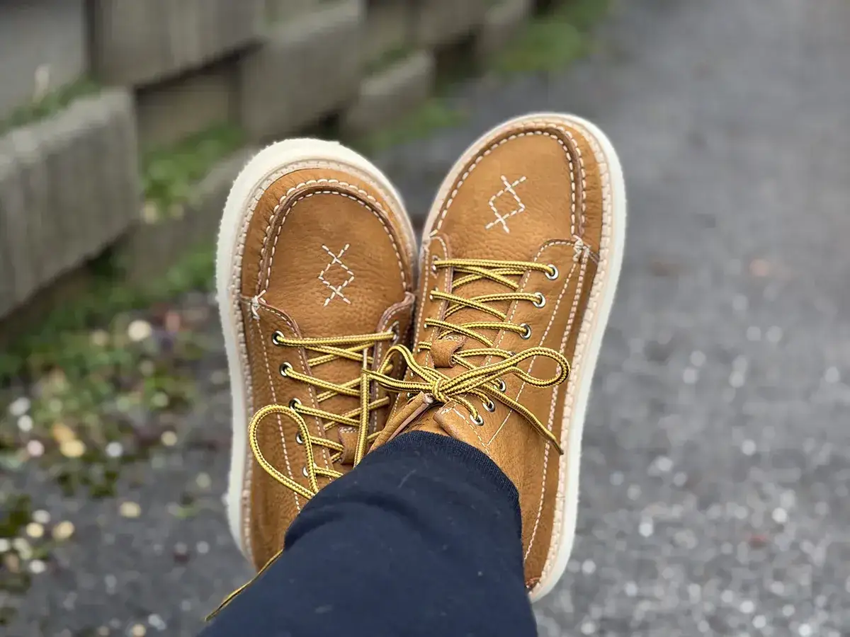 Par de zapatos de gamuza marrón con cordones amarillos y costuras blancas. Tienen un diseño de zapatos estrechos en la parte delantera.