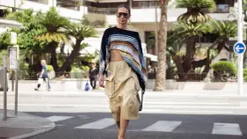 Mujer con un top corto de crochet y una falda vaporosa color beige, paseando por la calle con palmeras de fondo.