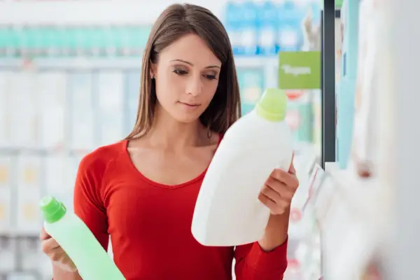Mujer compara dos botellas de detergente, leyendo la etiqueta producto de limpieza.