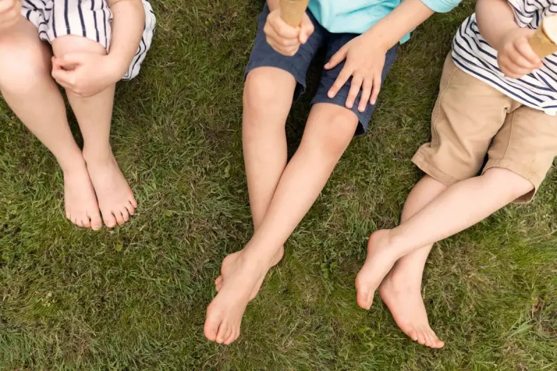 Niños sentados en el césped, uno con shorts talla 28 niño, disfrutando de un helado.