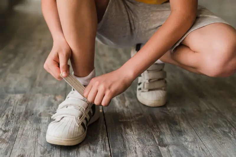 Niño se ata los cordones de sus zapatillas blancas. El número de pie según edad cambia rápido, ¡hay que estar al día!