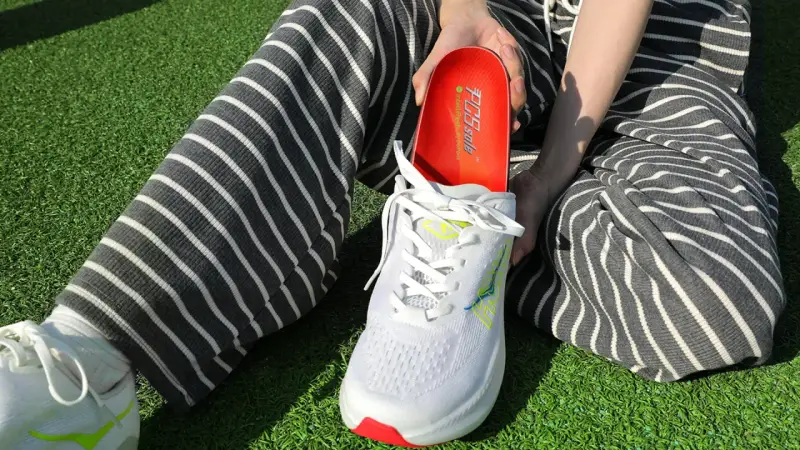Persona muestra una plantilla roja para el arco plantar, lista para ser colocada en un zapato deportivo blanco.