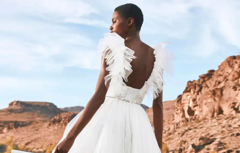 Novia con vestido blanco vaporoso, con volantes en los hombros, ideal para vestidos novia ibiza. Paisaje desértico al atardecer.